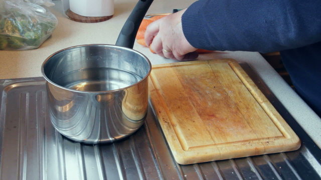 Middle-aged man in close up peeling the first of a small quantity of carrots in a domestic kitchen, prior to cooking them.