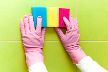 Hands in pink protective gloves cleaning tiles with colorful sponges. Early spring cleaning or regular clean up. Maid cleans house.
