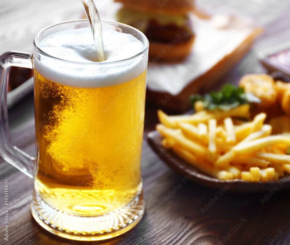 Wall mural glass mug of draft light beer with french fries on dark wooden table, close up