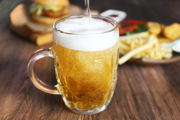 Glass mug of draft light beer with snacks on dark wooden table, close up