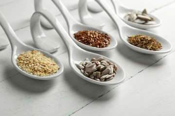 Different kinds of seeds in spoons on wooden table