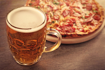 Tasty pizza and glass of beer are on wooden table, close up