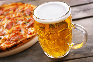 Tasty pizza and glass of beer are on wooden table, close up