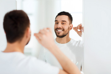 man cleaning ear with cotton swab at bathroom