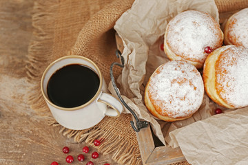 Delicious sugary donuts with red currant on wooden tray with parchment closeup
