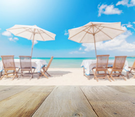 wooden table top with blur of table set and umbrella on the beach