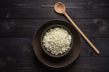 cottage cheese in a brown bowl on a dark wooden background