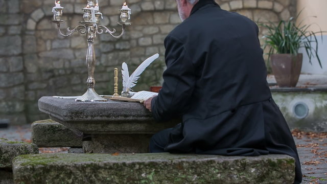 Man seats down at garden table to write a poem 