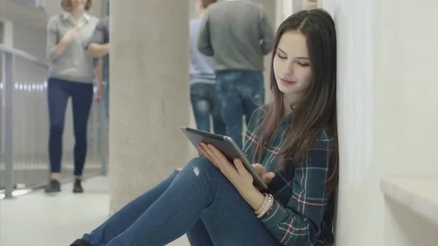 Portrait of a young attractive female student using a tablet computer while sitting in a college hallway. Shot on RED Cinema Camera.