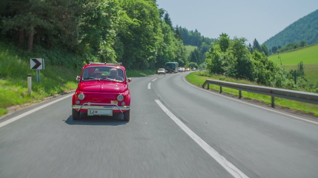 A queue of cars driving behind a vintage red zastava