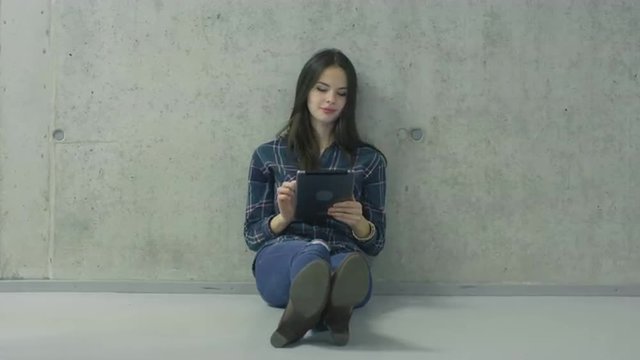 Young female students is sitting on the floor in a college hallway and using a tablet computer. Shot on RED Cinema Camera.
