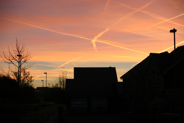 Sunset over houses with aircraft contrails