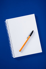 White spiral notepad with ball pen on blue background