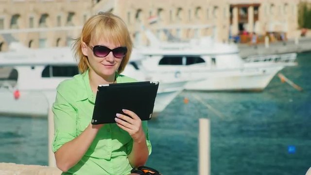 A female tourist enjoys the tablet against the backdrop of the bay with yachts