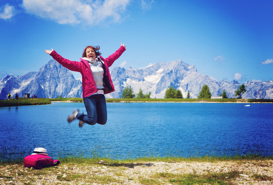 woman jumping beside a clear mountain lake enjoying the view