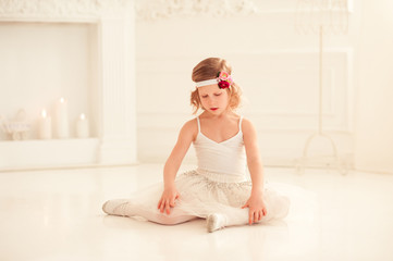 Beautiful baby girl sitting on white wooden floor. Wearing stylish white dress and floral hairband. Childhood. 