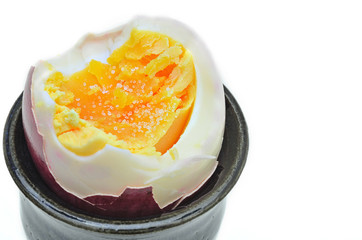 Hart gekochtes Ei, Makro / Ei, hart gekocht mit Salz, geköpft, angebissen, mit Sachale, rot, im Eierbecher, Makro, weißer Hintergrund, Querformat 