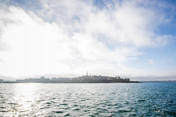 view of the fortified city of Saint-Malo behind behind the sea during a sunny day seen from a boat off the coast of brittany