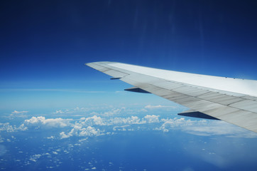 Obraz premium Wing of an airplane flying above the clouds over tropical island