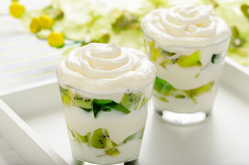 Healthy yogurt dessert with kiwi fruit, jell and cream in glass on white wooden tray.