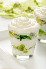 Healthy yogurt dessert with kiwi fruit, jell and cream in glass on white wooden tray.