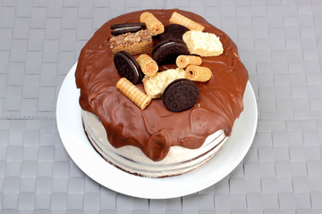 Cake, glazed with milk chocolate and decorated with waffles and cookies, on white plate