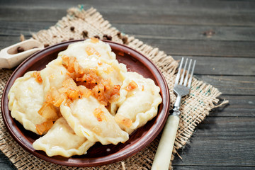 traditional Ukrainian and Russian cuisine , dumplings called varenyky of dough with cabbage, pepper and fat or salo in a clay plate on a dark wooden background