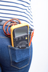 Electronic multimeter for electrician in back pocket of blue jeans worn by a woman. 
