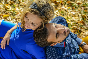 young pregnant couple sitting on yellow leaves in the park