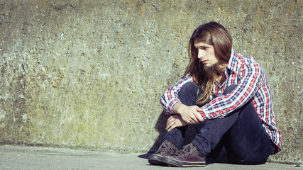 Man long haired sitting alone sad on grunge wall