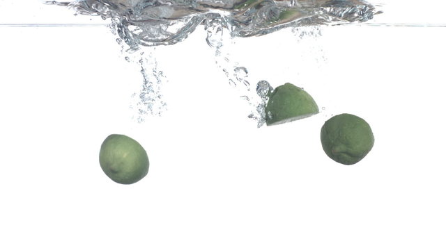 Limes splashing into water, slow motion