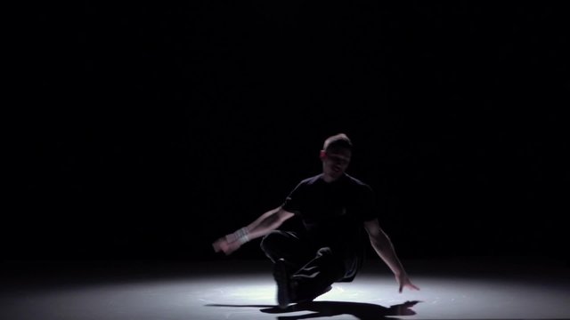 Dancer in dark suit starts dancing breakdance, on black, shadow, slow motion