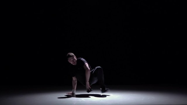 Dancer in dark suit continue dancing breakdance, on black, shadow, slow motion