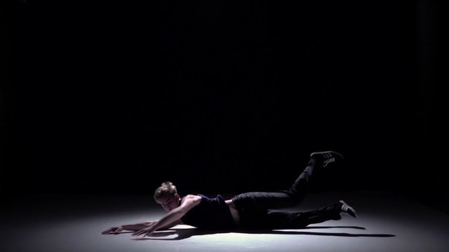 Handsome blonde dancer man dancing breakdance on black, slow motion