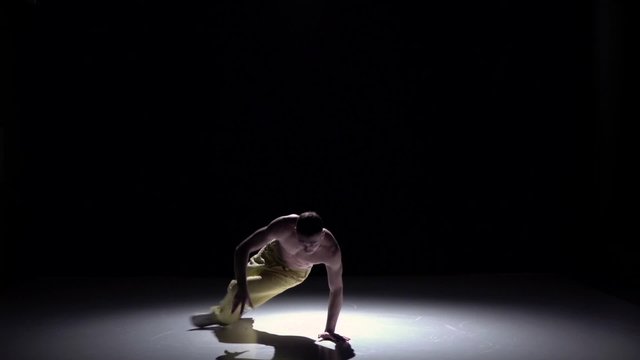 Breakdance dancer man in yellow trousers with naked torso starts dance on black, shadow, slow motion