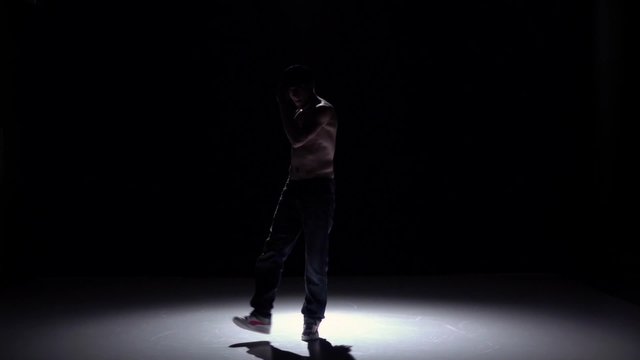 Breakdance dancer man in trousers, cap with naked torso dance on black, shadow, slow motion
