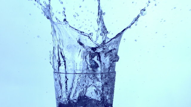 Ice splashing into a glass of water, slow motion