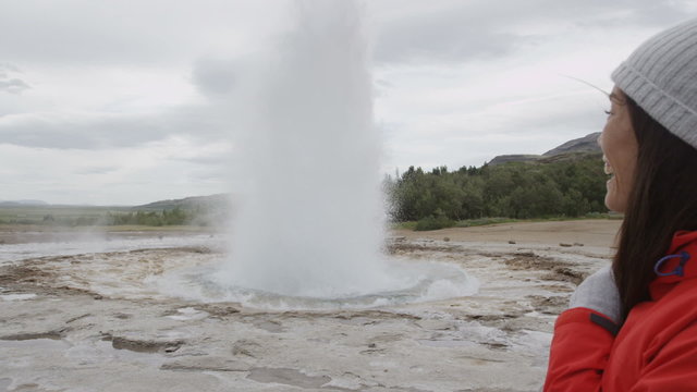 Iceland tourist by Strokkur geyser happy visiting famous tourist attractions and landmarks on the Golden Circle. Happy multiracial travel woman on holiday vacation sightseeing Icelandic nature.