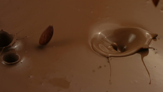 Almonds splashing into chocolate, slow motion