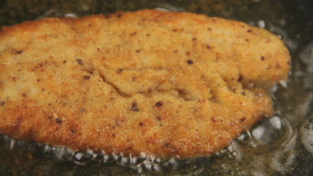 Close up pan across a ready crispy crumbed fish fillet frying in hot oil.