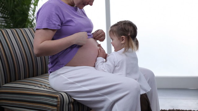 Young girl listens to mothers pregnant belly