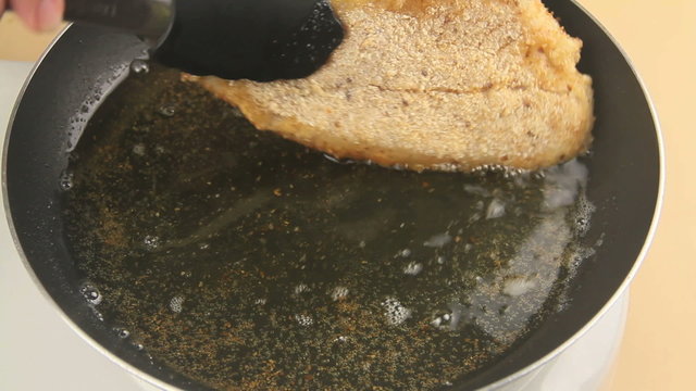 Turning a cooked fried fillet of crumbed fish with tongs in a pan of hot oil.