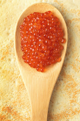 Red caviar on wooden spoon on pancake background