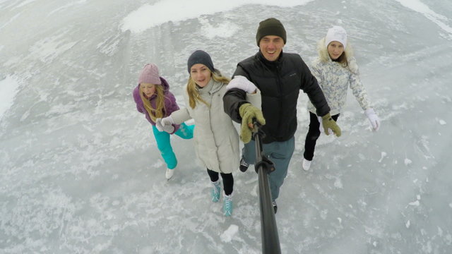 happy family taking picture with smartphone selfie stick and showing thumbs up on ice skating rink outdoors