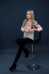 Attractive young blonde woman in transparent colorful blouse posing on gray background
