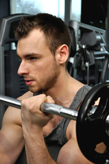 Fototapeta premium Mężczyzna na siłowni trzymający sztangę z obciążeniem.