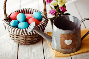 Multicolored Easter eggs in wicker basket on white wooden background
