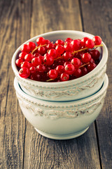 Fresh red currants in bowl on wooden background.