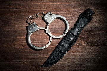 Knife and handcuffs on the wooden background. Criminal concept.