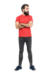 Young bearded guy in red t-shirt with crossed arms looking away. Full body length portrait isolated...